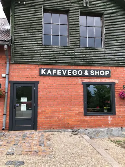 Sarkano ķieģeļu ēka ar tumšu koka augšstāvu un uzrakstu KAFEVEGO & SHOP virs loga
